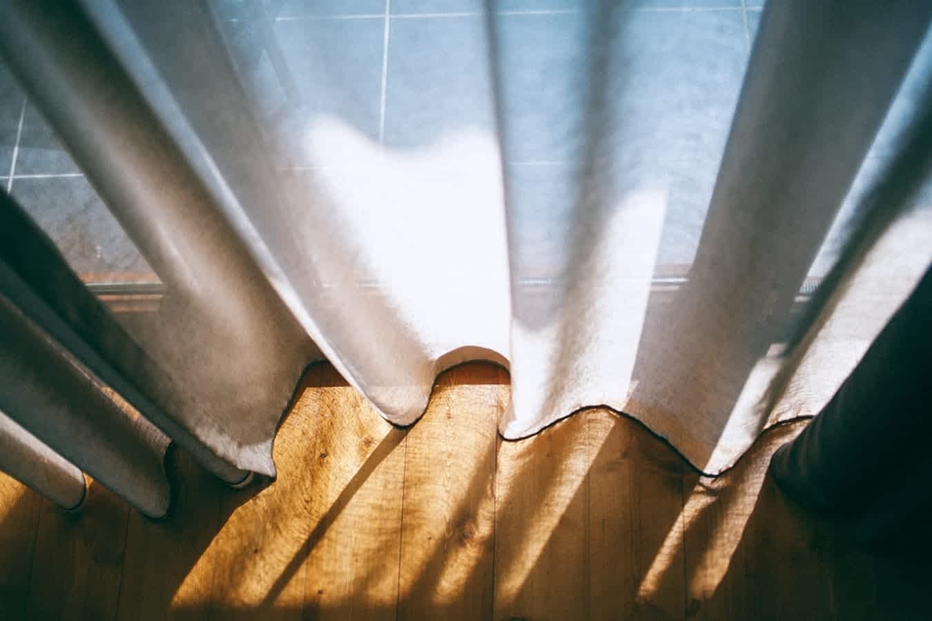 a blog asset photo of sun shining through white transparent curtains onto a hardwood floor