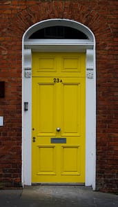 bright yellow door within a white frame against a brick wall