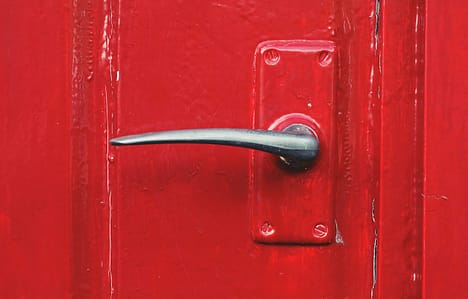 an old wooden door painted red. the photo is a close up of the door handle - which is a dark chrome colour.