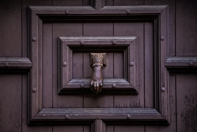 large brown oak door with metal borders, a metal door knocker in the shape of a hand hags in the middle of the frame