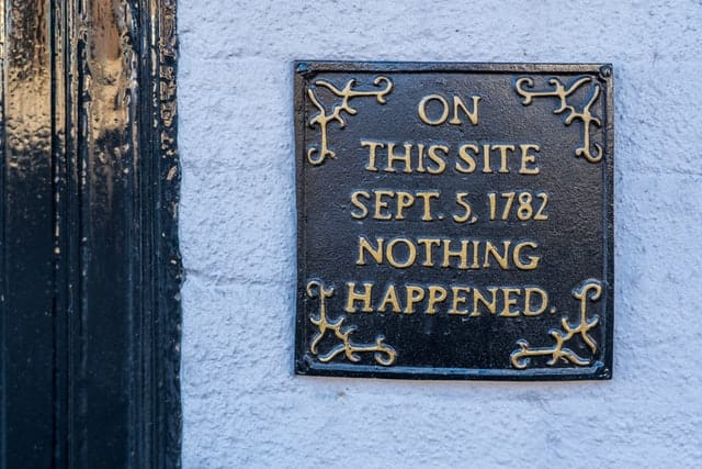 metal square plaque that reads on this site sept 5 1782 nothing happened on a white brick wall next door a black door frame