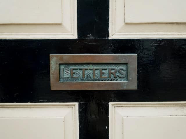 aged brass letterbox that reads letters on it, against a black and white door