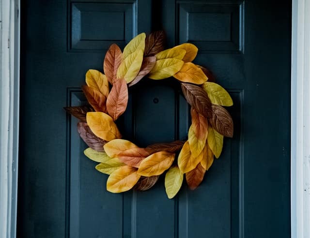 auburn, brown, and pale green leaves in the form of a wreath hanging from a dark blue door