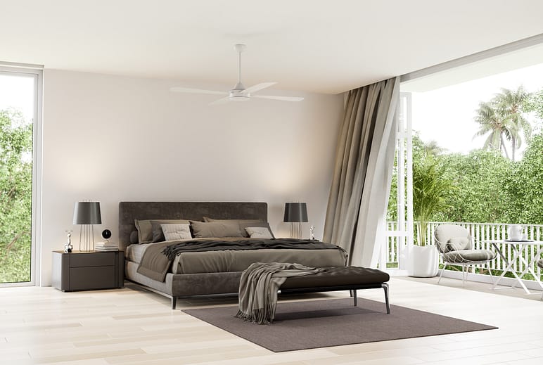 A large bright minimalist bedroom, featuring a grey and black contemporary looking bed with a grey carpet. The wall next to the bed opens up into a balcony. Almost the entire wall is opened via a set of bifolding doors. a set of sheer grey curtains flow in the wind.