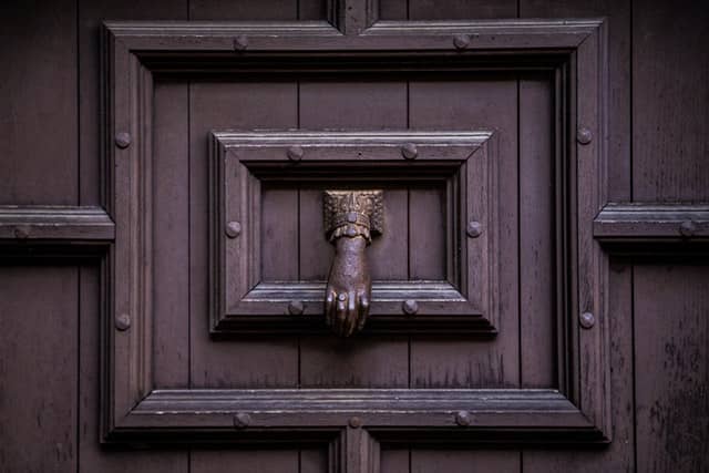 large brown oak door with metal borders, a metal door knocker in the shape of a hand hags in the middle of the frame