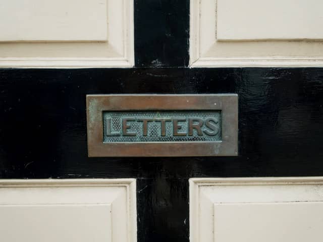 aged brass letterbox that reads letters on it, against a black and white door