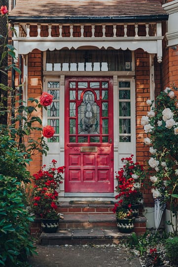 A red Edwardian door in porch with wooden cutout detailing.