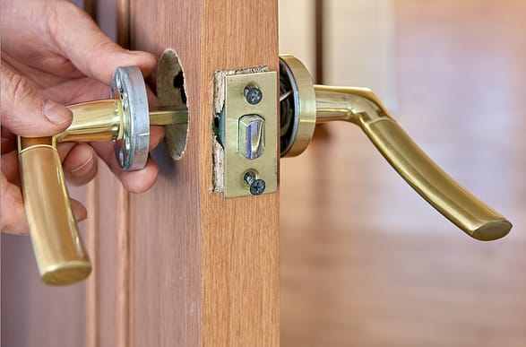 The image shows the side of a door with the latch tongue facing the camera. Two door handles are pulled from the door and hanging loosely, showing the inner workings of the door handle.